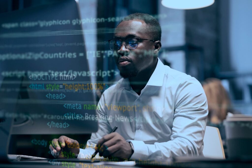 A man works at a computer, program code is in the foreground